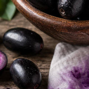 Frutas escuras com polpa roxa ao lado de tigela de madeira e tecido manchado